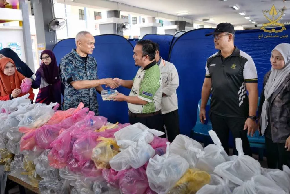 Mohamed Zahari (kiri) ketika menyerahkan juadah pelbagai menu kepada mangsa banjir di PPS Sekolah Kebangsaan Melati di sini hari ini. - Foto: FB Kesultanan Pahang