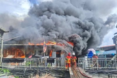 Anggota bomba bertungkus lumus memdamkan kebakaran rumah atas air di Kampung Pasir Putih, Putatan pada Isnin. 