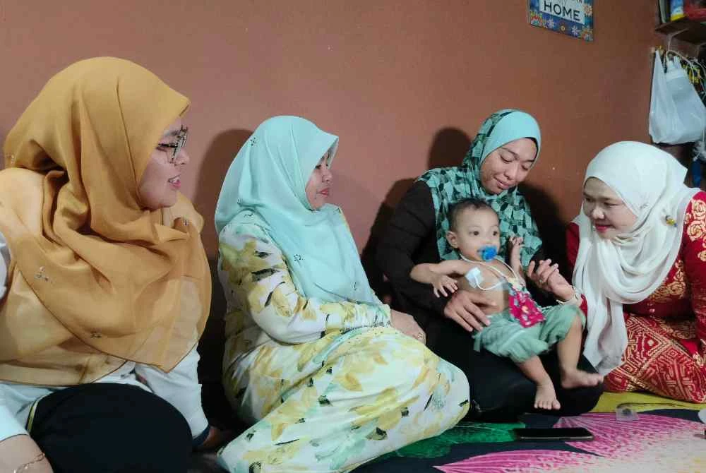 Salbiah (kanan) menyantuni Firas Affan ketika menziarahi keluarga berkenaan di Bandar Lahat Baru, Ipoh pada Selasa.