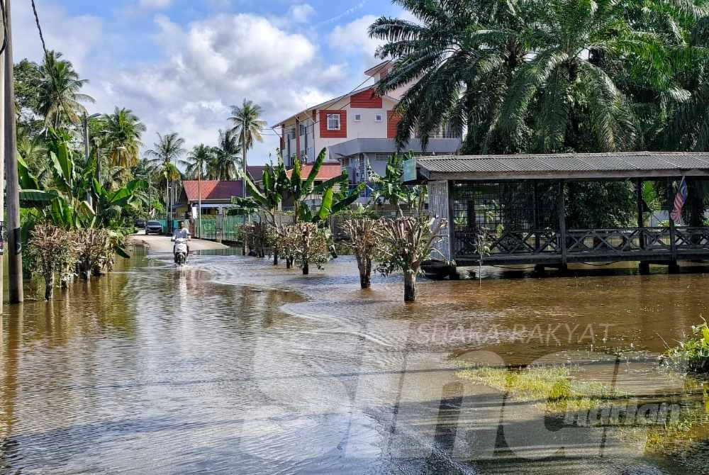 Penduduk melalui jalan kampung walaupun air masih bertakung.