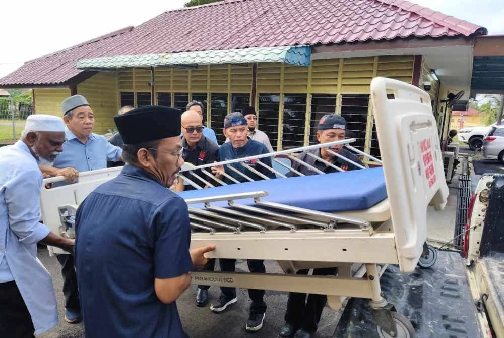 Wakil pengurusan kariah dan ahli Tiga Abdul mengangkat katil hospital untuk dihantar kepada pihak memerlukan.