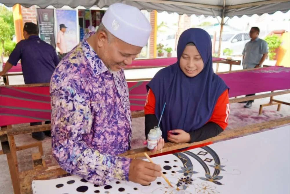 Afizah menunjukkan kaedah menghasilkan batik ketika menerima lawatan Exco Keusahawanan, Sumber Manusia, Koperasi dan Hal Ehwal Pengguna negeri Terengganu, Ariffin Deraman (kiri) di bengkelnya yang terletak di Kampung Raja, Besut.
