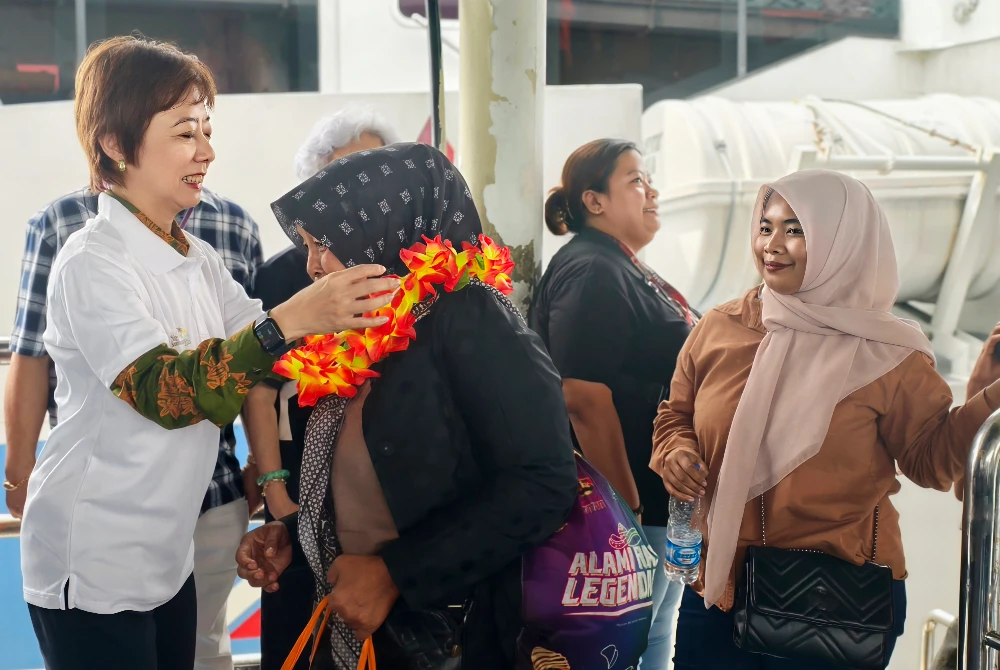 Nicole menyarung kalungan bunga pada pelancong Indonesia yang tiba di Jeti Penumpang Port Dickson pada Khamis.