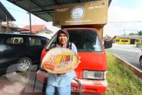 Nor Aini memegang kek lapis di hadapan food truck yang akan dihadiahkan kepada pelanggan bertuah.