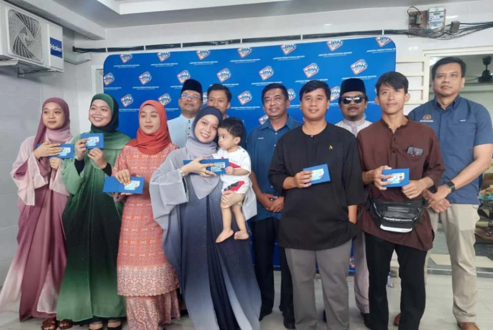 Nur Hakika (depan, dukung bayi) dan enam lagi adik beradiknya menerima kad pengenalan yang disampaikan Badrul Hisham (belakang, tengah) pada majlis penyerahan di rumah mereka di Bandar Sungai Buaya, Rawang pada Jumaat.