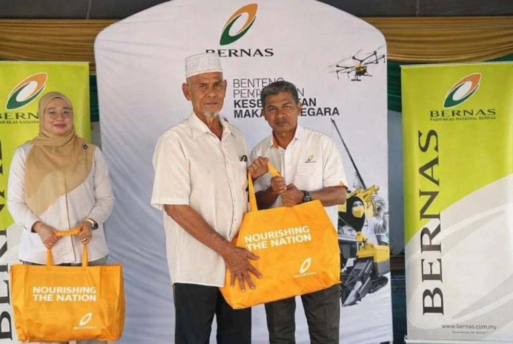 Haslizan (kanan) menyampaikan sumbangan kepada penerima bantuan Program Ikhlas BERNAS Pasca Banjir di Simpang Empat, Perlis.