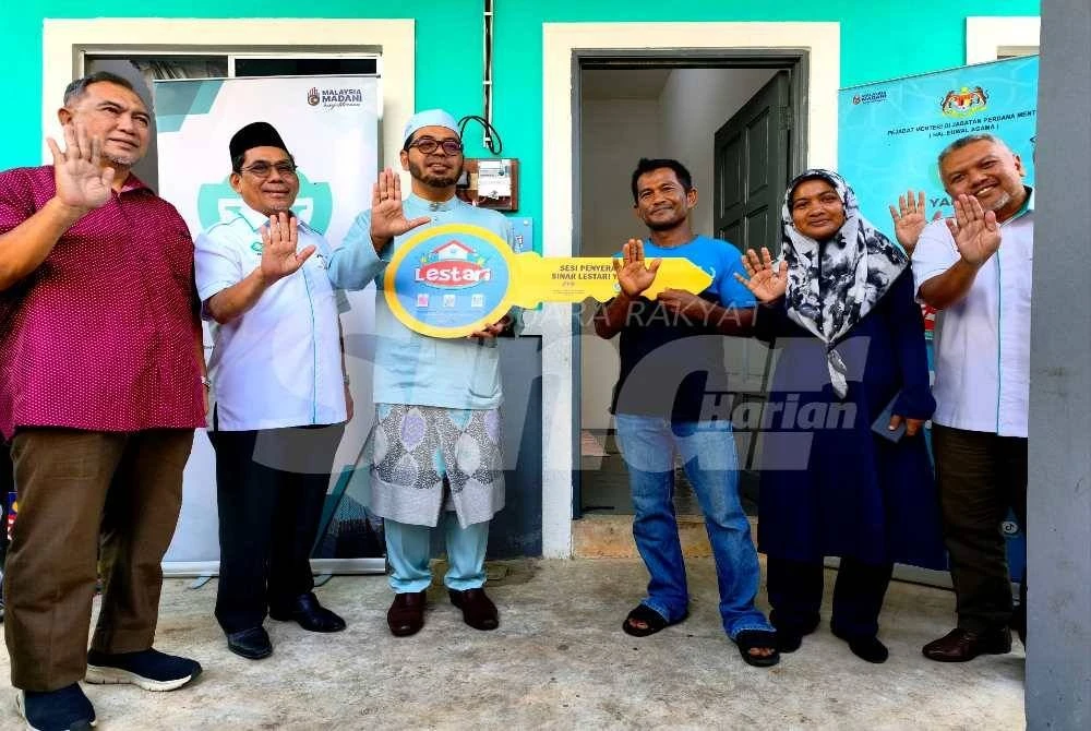 Zulkifli (tiga dari kiri) menyerahkan simbolik kunci rumah kepada Mohd Azhar Mat Hussin (tiga dari kanan) dan isteri pada Sesi Penyeraham Sinar Lestari YaPEIM di Kampung Aman, Kandis, Bachok pada Jumaat.