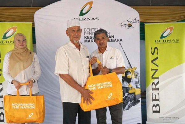 Haslizan (kanan) menyampaikan sumbangan kepada penerima bantuan Program Ikhlas BERNAS Pasca Banjir di Simpang Empat, Perlis.