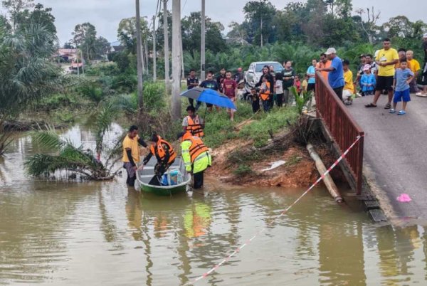 Anggota polis membantu memindahkan penduduk berisiko menggunakan bot selepas jambatan menghubung Kampung Sungai Mok runtuh pada Jumaat. Foto: Polis Rompin