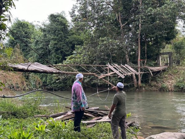 Mohd Zaki (kanan) bersama Fauzi meninjau keadaan terkini titi gantung yang runtuh di Sungai Chatel Damai, Lata Rek, Kuala Krai pada Sabtu. 