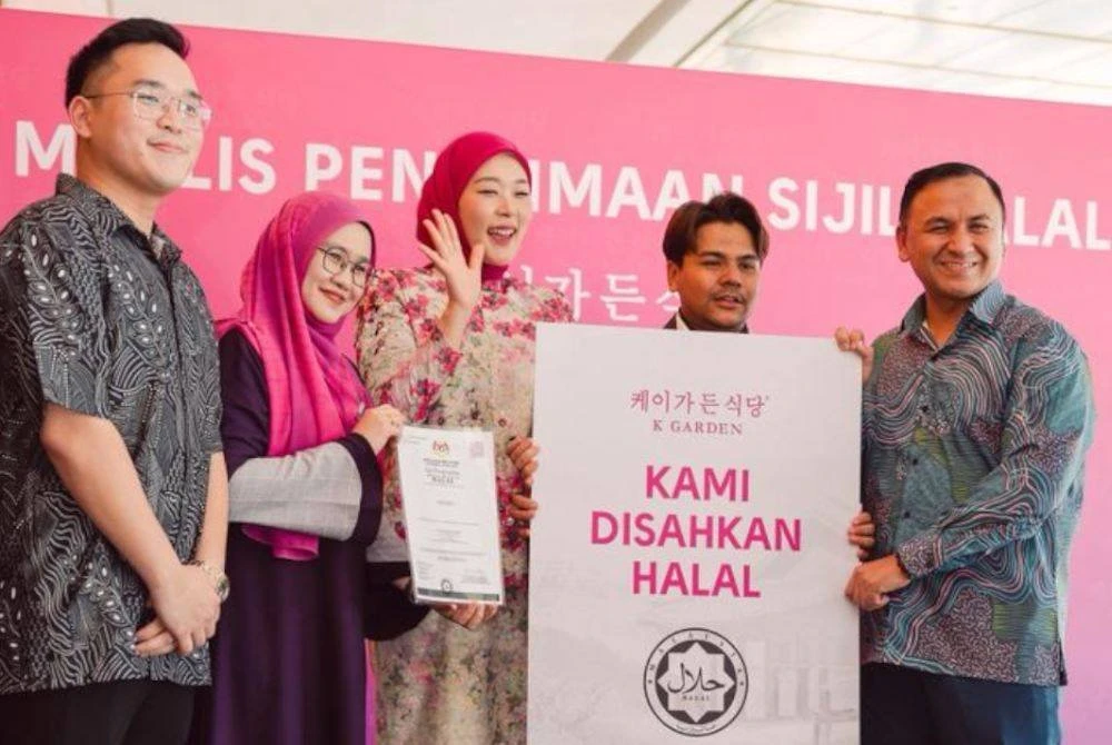 USTAZ IMRAN menyerahkan replika logo halal Jakim kepada Ryzal dan Maryam pada Majlis Penerimaan Sijil Halal K Garden baru-baru ini.