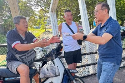 Dominic (kanan) mengedarkan kalendar kepada orang awam di Pasar Awam Sungai Ara pada pagi Sabtu.