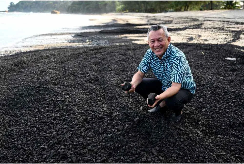 Razali meninjau bahan pepejal berwarna hitam, dipercayai arang batu, yang terdampar di Pantai Teluk Kalong dekat sini. - Foto: Bernama