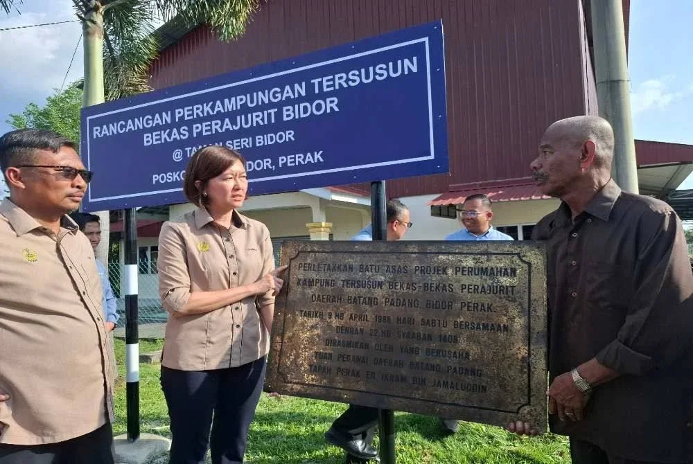 Sandrea bersama Mohamad Yusri (kiri) melihat papan tanda peletakan batu asas projek perumahan kampung tersusun bekas-bekas perajurit daerah Batang Padang di Bidor yang bertarikh 1988.