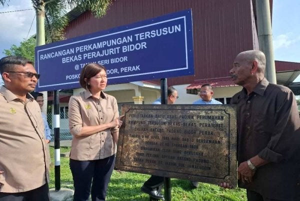 Sandrea bersama Mohamad Yusri (kiri) melihat papan tanda peletakan batu asas projek perumahan kampung tersusun bekas-bekas perajurit daerah Batang Padang di Bidor yang bertarikh 1988.