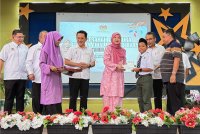 Fadhlina (empat dari kanan) menyampaikan BAP kepada salah seorang murid di Majlis Penyerahan Cek Cura BAP kepada Jabatan Pendidikan Negeri Pulau Pinang dan Pejabat Pendidikan Daerah di Sekolah Menengah Kebangsaan Tun Syed Barakbah, Nibong Tebal pada Selasa.