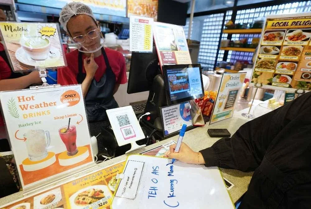 Pelanggan menulis permintaan ‘kurang manis’ pada papan putih kecil, antara kaedah komunikasi tanpa lisan yang digunakan di DIB bagi memudahkan urusan pesanan.