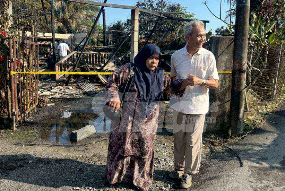 Siti Haminah (kiri) dipimpin suaminya keluar dari kawasan rumah mereka yang hangus. - Foto Sinar Harian/Adila Sharinni Wahid
