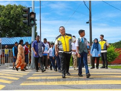 Alexander bersama seorang pelajar melintas jalan raya selepas menggunakan lampu isyarat baharu yang disediakan. 