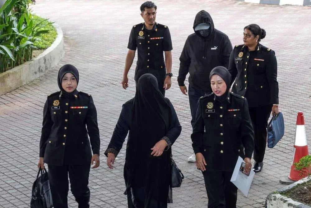  Pegawai Imigresen Gred KP22, Mohamad Fadzli Abdul Rahim, 46, dan isterinya, Suhana Ismail, 45, diiringi pegawai Suruhanjaya Pencegahan Rasuah Malaysia (SPRM) ketika dibawa ke Mahkamah Sesyen Shah Alam hari ini bagi menghadapi pertuduhan rasuah dan pengubahan wang haram. Foto Bernama 