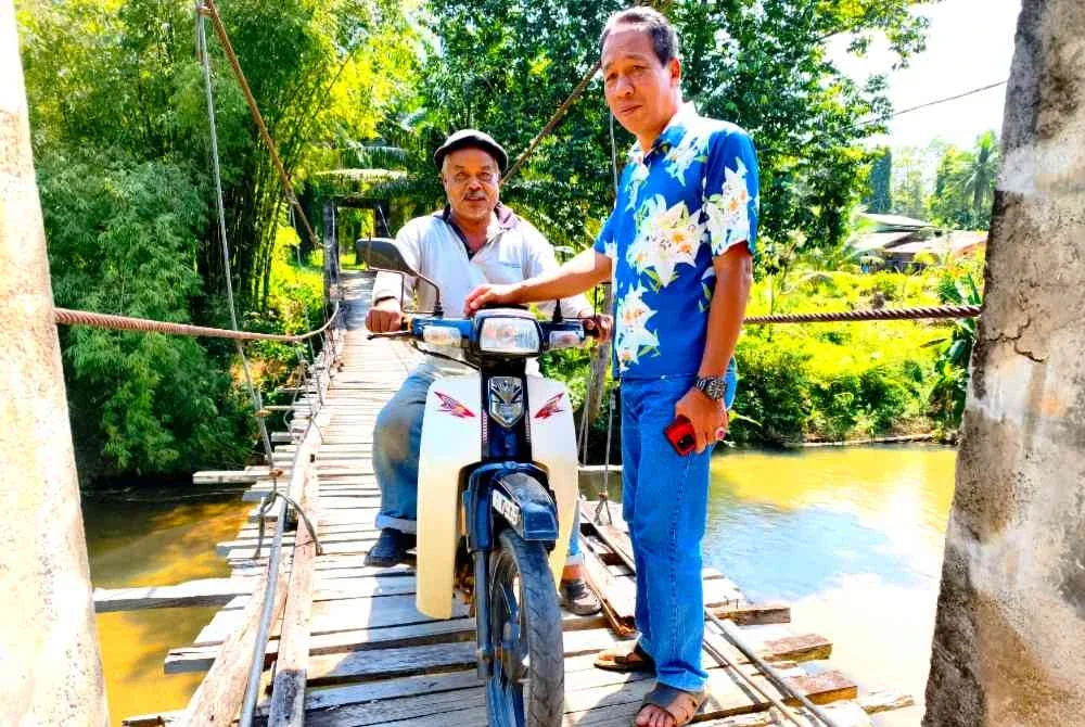 Mohd Zamri (kanan) semasa meninjau keadaan terkini jambatan gantung di Jelekis, Lata Rek, Kuala Krai. - Foto Sinar Harian/Hazelen Liana Kamarudin