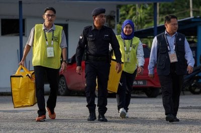 Petugas SPR membawa beg berisi kotak undi dengan diiringi pihak polis setelah proses pengundian awal bagi PRK Parlimen Kinabatangan dan DUN Lamag di Teratak Ibu Pejabat Polis Daerah Kinabatangan tamat tepat jam 5 petang pada Selasa. Foto: Bernama 