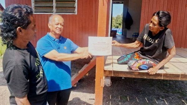 Osman (tengah) dan Anuar (kiri) bersama seorang penduduk menunjukkan notis arahan pengosongan tanah yang diterima daripada Pejabat Daerah dan Tanah Dungun baru-baru ini.