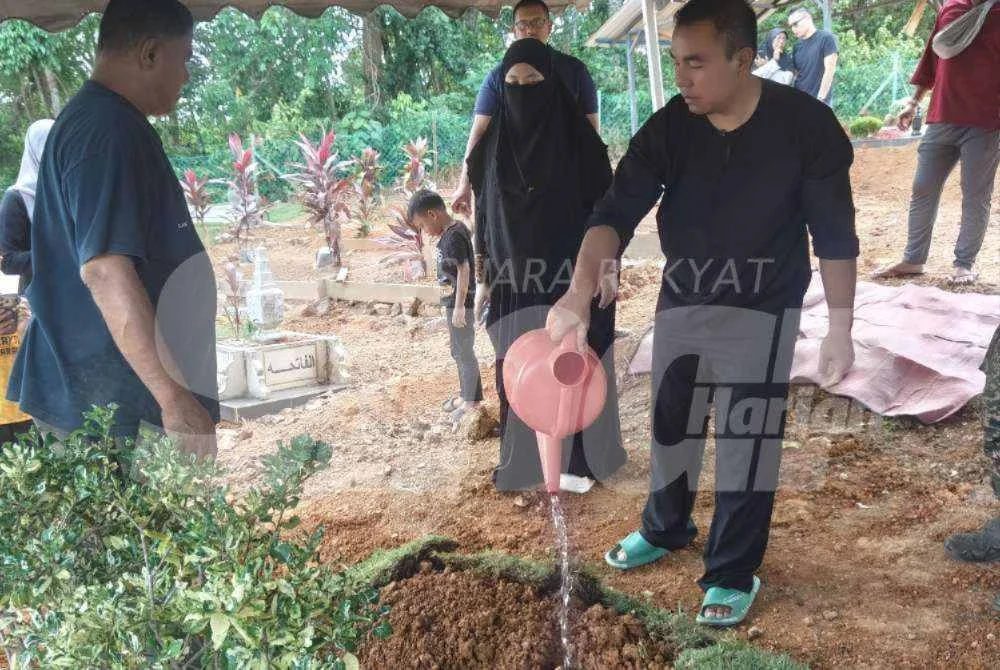 Mohd Fikry (kanan) menyiram air di pusara anaknya, Maryam Al Khawla.