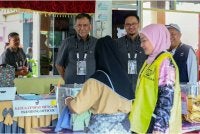 Ramlan (kiri) melihat seorang pengundi memasukkan kertas undi ke dalam peti undi sewaktu meninjau proses pengundian bagi PRK Parlimen Kinabatangan dan DUN Lamag di Sekolah Kebangsaan Bukit Garam II pada Sabtu. Foto Bernama