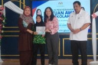 Nie Ching (dua, kanan) menyempurnakan gimik penyerahan Bantuan Awal Persekolahan kepada salah seorang penerima di SK Putra Utama pada Isnin.