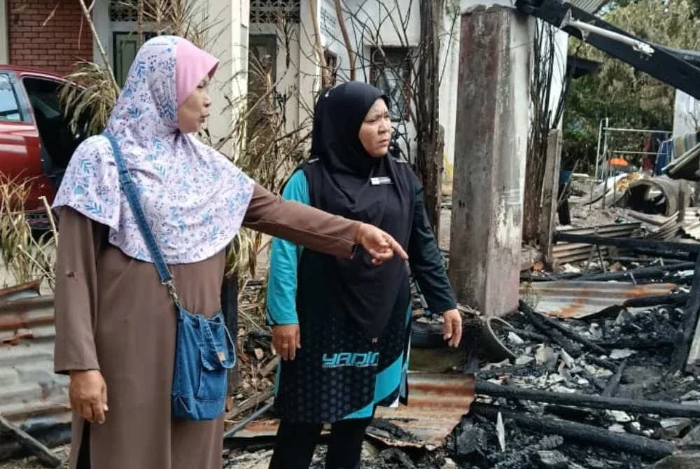 Norhaeda (kiri) menunjukkan lokasi di mana dia menempatkan sangkar-sangkar kucing yang dipelihara kepada Yusnita di tapak rumahnya yang terbakar di Jalan Tok Guru, Kota Bharu pada Rabu. Foto: Yadim