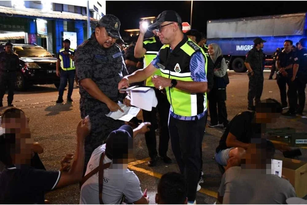 Khairrul Aminus (kanan) memeriksa dokumen warga asing dalam serbuan Op Sapu di sekitar Kepong pada Khamis.