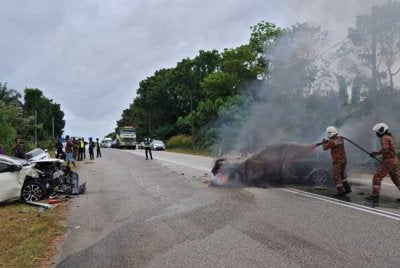 Anggota bomba memadamkan kebakaran kereta Persona selepas terlibat dalam kemalangan empat kenderaan di Kilometer 43, sempadan Mersing. - Foto JBPM Johor
