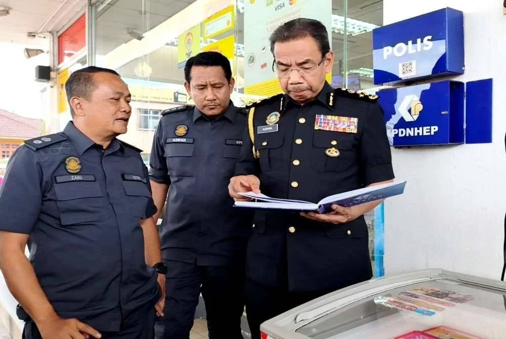 Azman (kanan) memeriksa buku di salah sebuah stesen minyak di Rantau Panjang semasa sesi lawatan kerja beliau pada Ahad