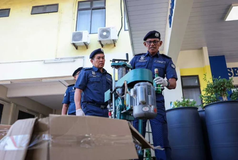 Rohaizad (kanan) menunjukkan peralatan memproses minuman keras yang berjaya dirampas dalam satu operasi di Sungai Dua. Foto Bernama