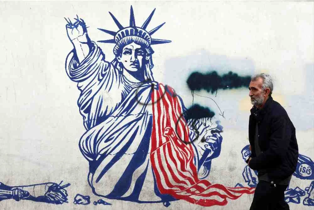 Seorang lelaki berjalan melepasi mural Patung Liberty Amerika Syarikat dengan lengan memegang obor patah di bekas bangunan Kedutaan AS di Teheran. Foto: AFP