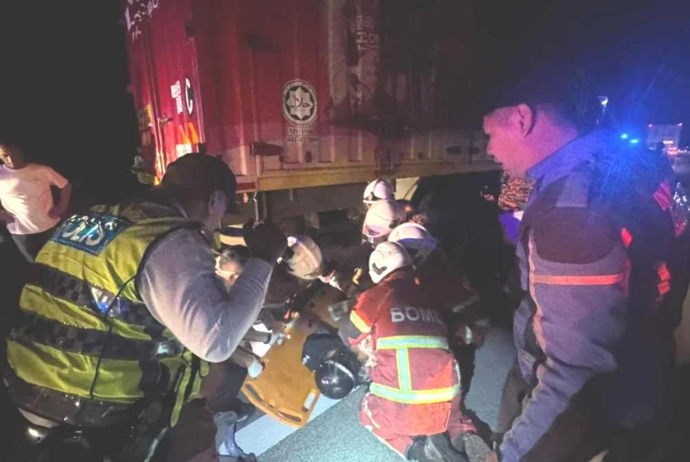 Anggota bomba berusaha mengeluarkan mangsa yang terperosok di bawah lori. Foto ihsan polis