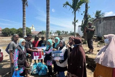 Robaatun Hadayiah (enam dari kanan) menyerahkan sumbangan al-Quran kepada salah seorang mangsa banjir terlibat ketika misi bantuan kemanusiaan ke Aceh, Indonesia baru-baru ini.