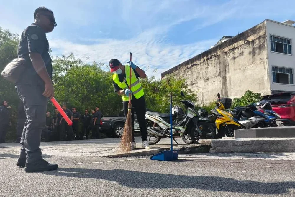 Mohd Hashim dan Herrykurniawan menyapu sampah di kawasan Nilai sebagai denda bagi kesalahan membuang puntung rokok merata-rata.
