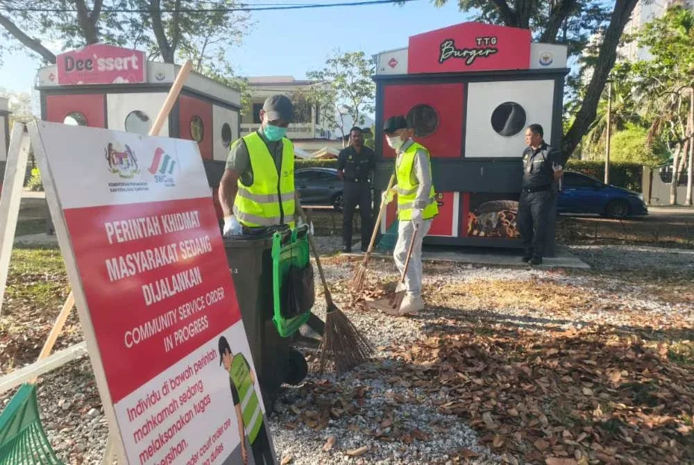Anggota penguatkuasa SWCorp memantau dua lelaki yang mengaku bersalah membuang sampah di tempat awam melaksanakan PKM di kawasan Stadium Darul Aman pada Jumaat.