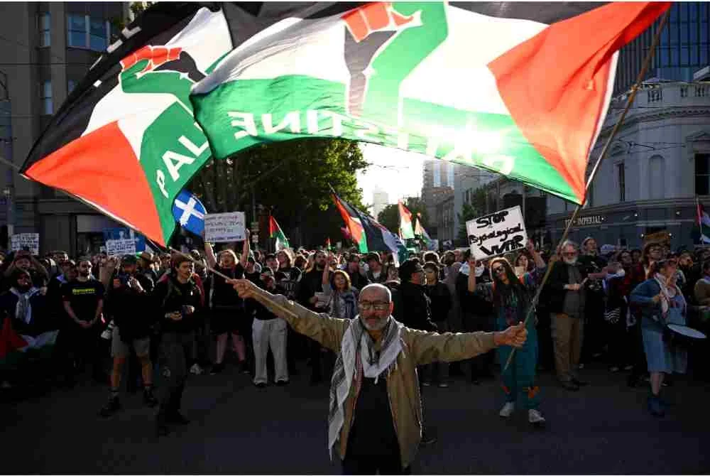 Penunjuk perasaan mengibarkan bendera dan mengangkat papan tanda semasa berarak ketika membantah lawatan Presiden Israel di Melbourne.