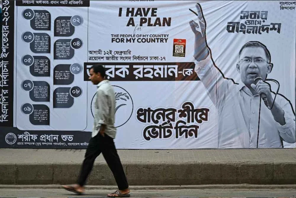 Seorang lelaki berjalan melepasi poster kempen Tarique, di luar pejabatnya di Dhaka.-AFP