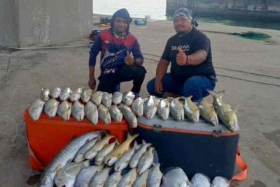 Khairul Adha (kanan) menunjukkan hasil tangkapan yang diperoleh dengan memancing dibawah Jambatan Pulau Pinang.