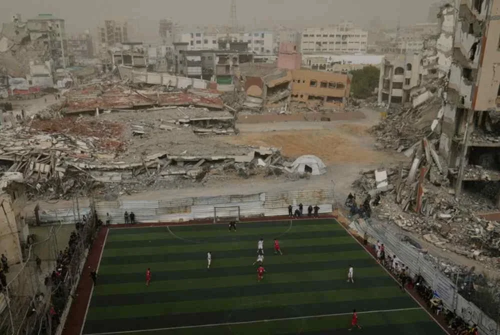 Pemain dari pasukan Kelab Sukan Gaza dan Kelab Al-Ahly mengambil bahagian dalam pertandingan bola sepak di padang yang dikelilingi bangunan yang musnah akibat serangan udara Israel di Gaza City. Foto Agensi