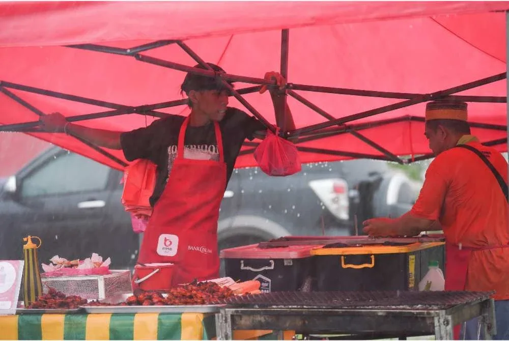 Salah seorang peniaga menahan khemah bagi mengelakkannya terbang susulan hujan lebat dan angin kencang. FOTO: Rosli Talib 