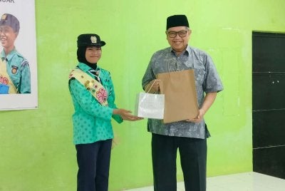 Lat menerima cenderahati daripada calon Anugerah Pandu Puteri Raja, Aysha Zahra Anuar sempena Program Khidmat Masyarakat Semaian Kasih Persatuan Pandu Puteri Malaysia Cawangan Perak di Maahad Darus Salam, Rizab Kampung Melayu Tambun di sini pada Jumaat.