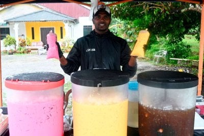 Bekas pemain kebangsaan Harimau Malaya dan pasukan JDT, Mohammad Gopi Rizqi, 37, sebelum ini dikenali sebagai R. Gopinathan, menunjukkan air jagung dan air sirap bandung cincau antara minuman balang yang dijualnya sempena bulan Ramadan di hadapan rumahnya di Kampung Api-Api. Foto: Bernama
