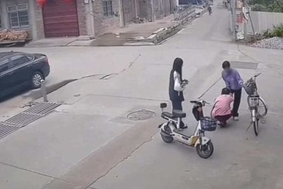 Tangkap layar video CCTV menunjukkan dua pelajar berkenaan sedang membantu mangsa yang terjatuh dari basikal. Foto: Agensi