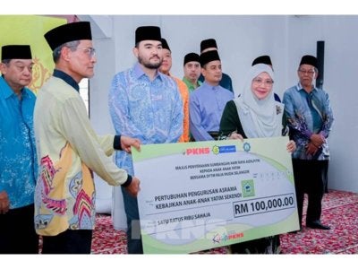 Sapna (kanan) menyerahkan simbolik cek kepada Ahmad Bustamam Abdul Latiff (kiri) sambil disaksikan Raja Muda Selangor, Tengku Amir Shah pada Majlis Penyerahan Sumbangan Hari Raya di Asrama Kebajikan Anak-Anak Yatim Miskin Sekendi di sini pada Sabtu.