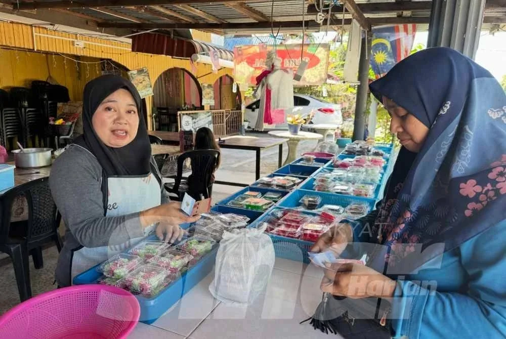 Nor Maziah (kanan) membayar kuih-muih RM1 yang dibeli di gerai Ros Asmarizan (kiri). Foto: ADILA SHARINNI WAHID